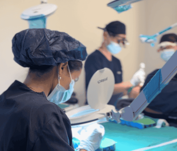 Medical team wearing masks and gloves performing a procedure under bright lights. Doctors and assistants working in a sterile environment.